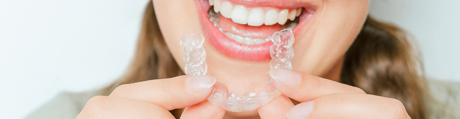 Woman holding clear aligner in front of smile.